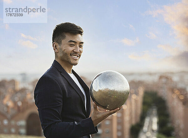 Happy young man holding silver ball at sunset
