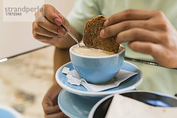 Hands of man dipping cookie in coffee cup