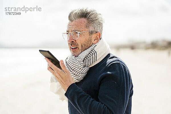 Reifer Mann mit Schal telefoniert am Strand