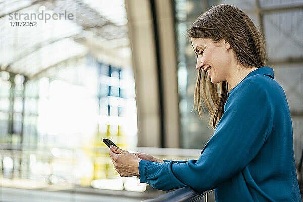 Lächelnde Geschäftsfrau benutzt Mobiltelefon im Büroflur