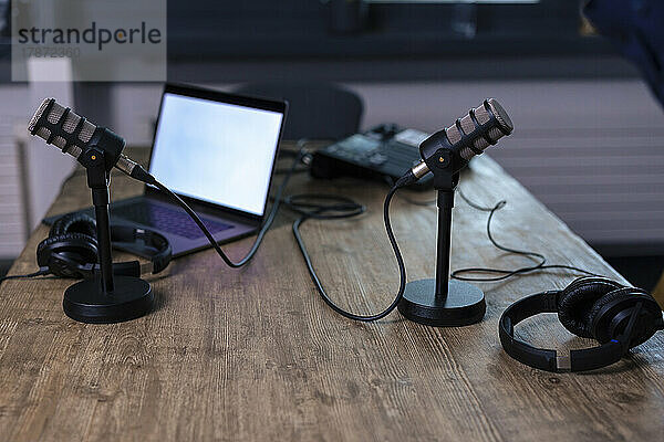 Microphones with headset and laptop on desk in recording studio