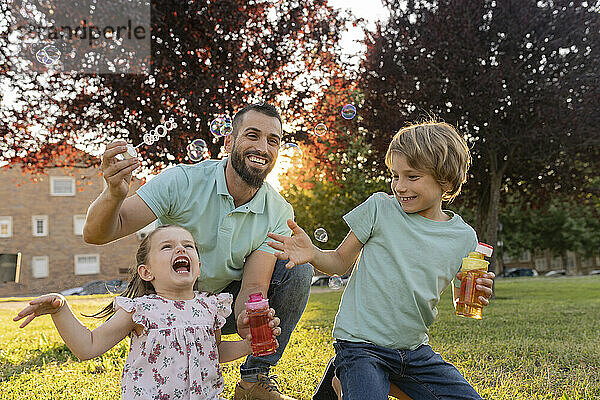 Kinder und Vater spielen mit Seifenblasen im Park