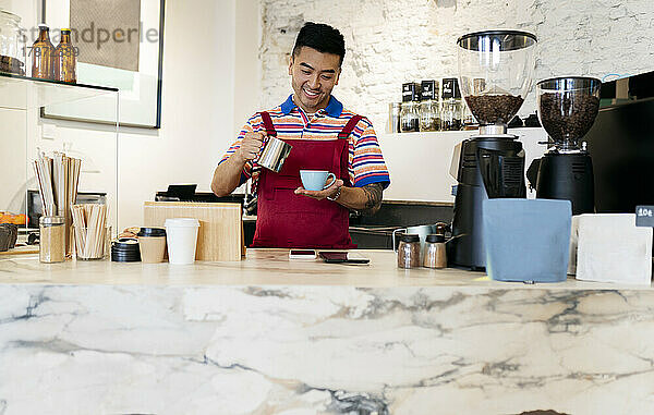 Lächelnder junger Mann mit Kaffeetasse und Tasse  der im Café arbeitet