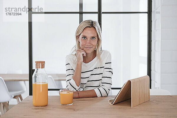 Junge Frau mit Saftglas und Tablet-PC auf dem heimischen Tisch