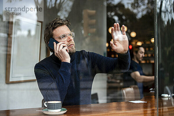 Geschäftsmann spricht mit Smartphone und berührt Glasfenster eines Cafés