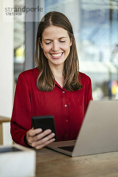 Smiling businesswoman using smart phone at work place