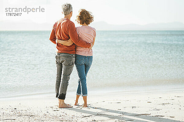 Liebevolles reifes Paar mit Armen umeinander  das am Ufer des Strandes steht