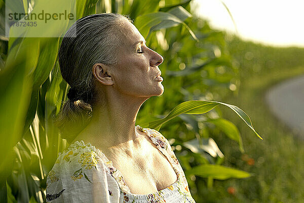Ältere Frau mit geschlossenen Augen steht vor einem Maisfeld