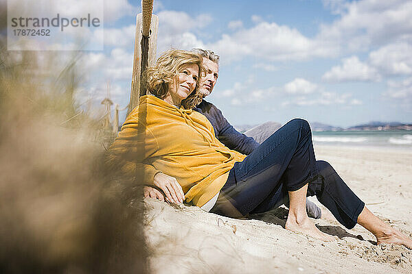 Glücklicher reifer Mann und Frau sitzen an einem sonnigen Tag am Strand