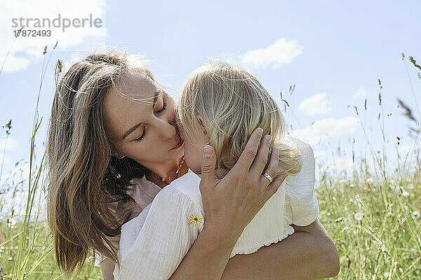 Mother kissing daughter on sunny day at field