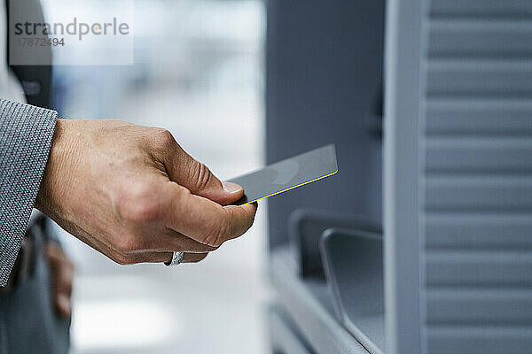 Hand eines Geschäftsmannes mit Kreditkarte in der Nähe eines Geldautomaten