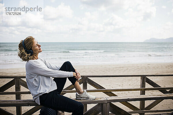 Glückliche Frau mit kabellosen Kopfhörern  die am Strand Musik hört
