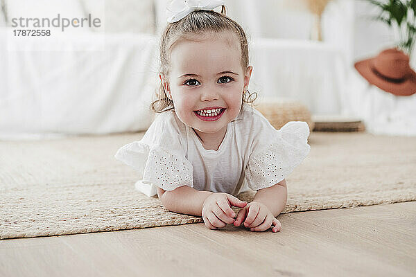 Nettes kleines Mädchen  das zu Hause auf dem Teppich liegt