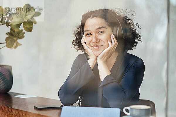 Lächelnde Frau mit Kopfhörern sitzt am Tisch im Café