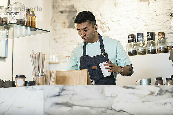 Man holding disposable coffee cup working in cafe