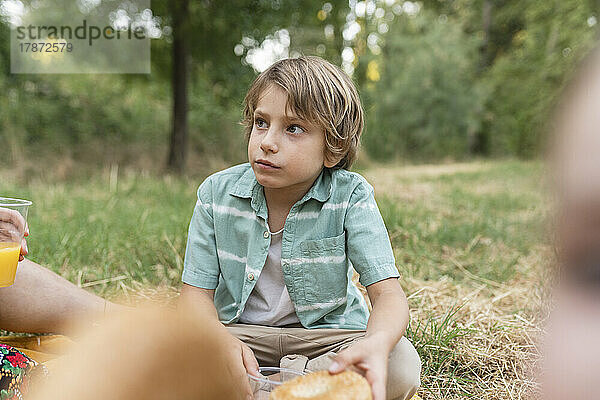 Junge hält Brot im Park sitzend