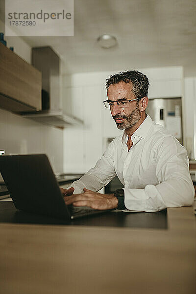Reifer Geschäftsmann benutzt Laptop auf der Küchentheke zu Hause