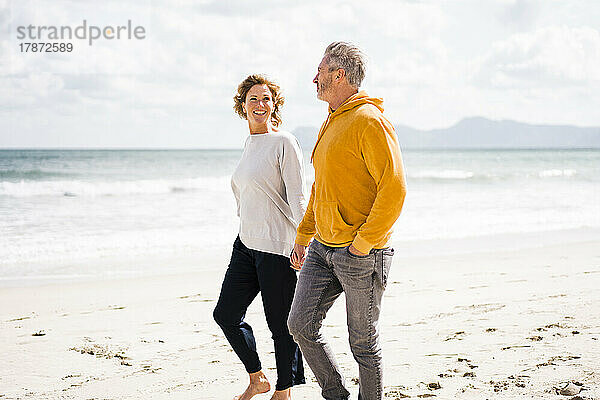 Mature man with woman walking on shore at beach
