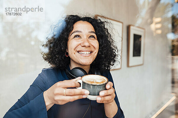 Glückliche Frau mit Kaffeetasse  gesehen durch Glas im Café