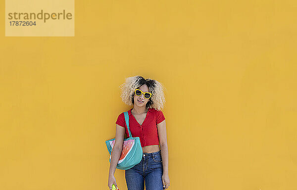 Junge Frau mit Sonnenbrille steht vor gelber Wand