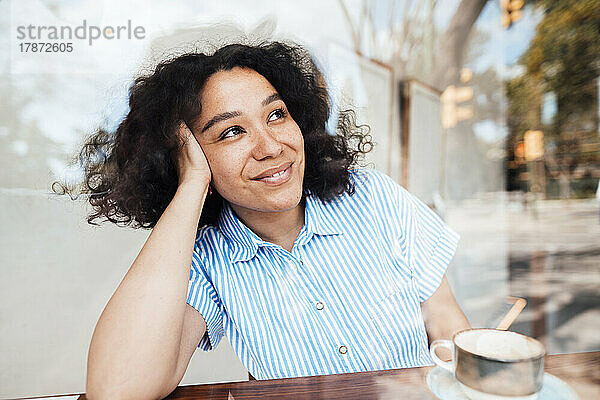 Lächelnde Frau mit Kaffeetasse sitzt am Tisch im Café