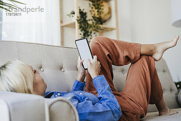 Frau benutzt Smartphone auf Sofa zu Hause