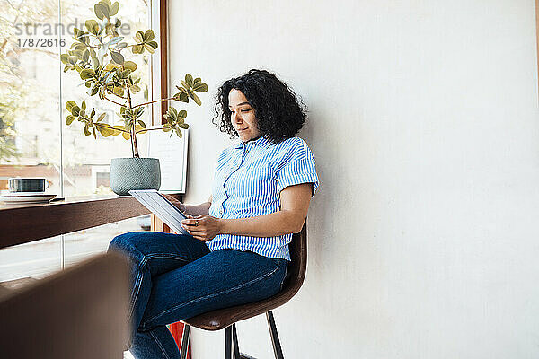Frau sitzt mit Tablet-Computer auf Stuhl im Café