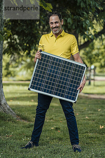 Glücklicher Mann hält Solarpanel im Park