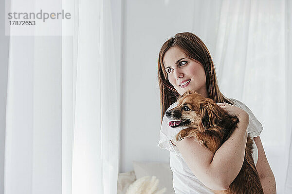 Smiling woman carrying dog at home