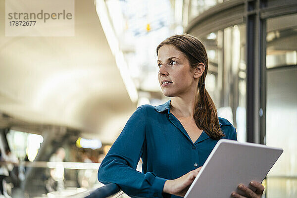 Nachdenkliche Geschäftsfrau mit Tablet-PC am Geländer im Büro