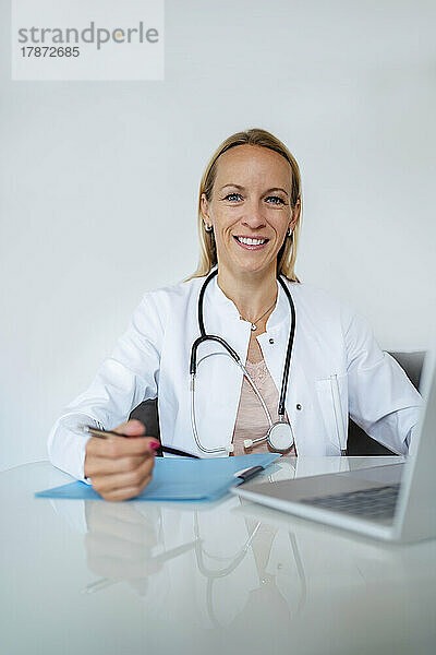 Porträt einer lächelnden Ärztin am Schreibtisch in der Arztpraxis