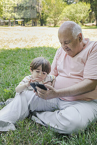 Großvater und Enkel nutzen Smartphone im Park