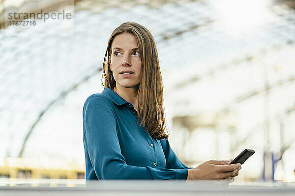 Nachdenkliche Geschäftsfrau mit Smartphone im Büro