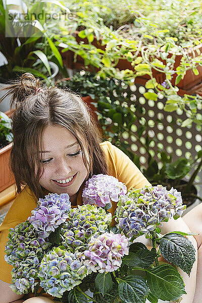 Lächelndes Teenager-Mädchen blickt auf Hortensienblüten auf dem Balkon