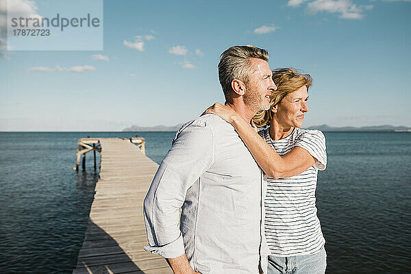 Lächelnde Frau und Mann stehen am Steg vor dem Meer