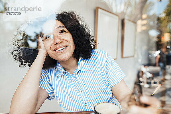 Glückliche Frau mit Kaffeetasse sitzt am Tisch im Café