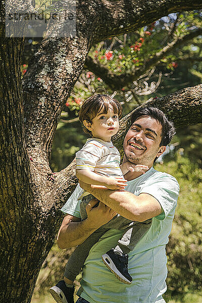 Glücklicher Vater mit Sohn  der vor einem Baum im Park steht