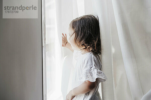 Kleines Mädchen schaut zu Hause aus dem Fenster