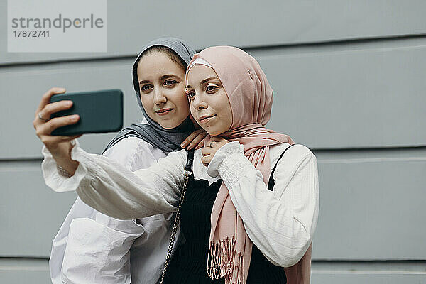 Young woman with friend taking selfie through smart phone