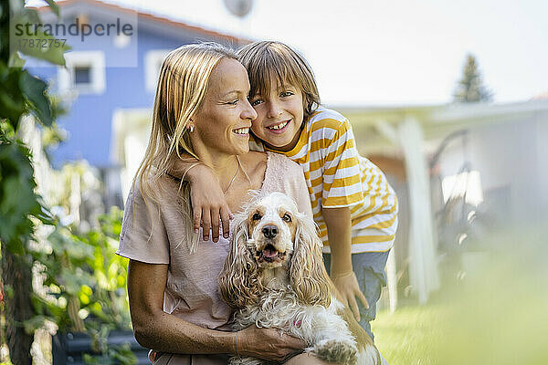 Porträt einer lächelnden Mutter und ihres Sohnes mit Hund im Garten
