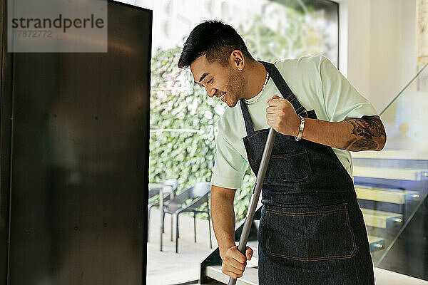 Smiling man with broom cleaning in coffee shop