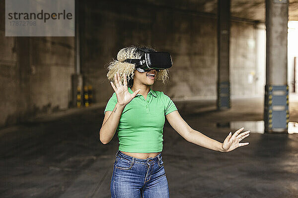 Lächelnde Frau mit Virtual-Reality-Simulator gestikuliert im Parkhaus