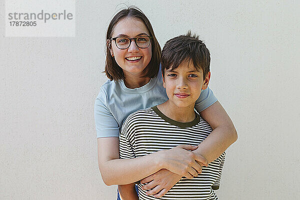Lächelnde Mutter umarmt Sohn vor weißer Wand