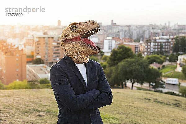 Junger Geschäftsmann mit Dinosauriermaske steht auf einem Hügel
