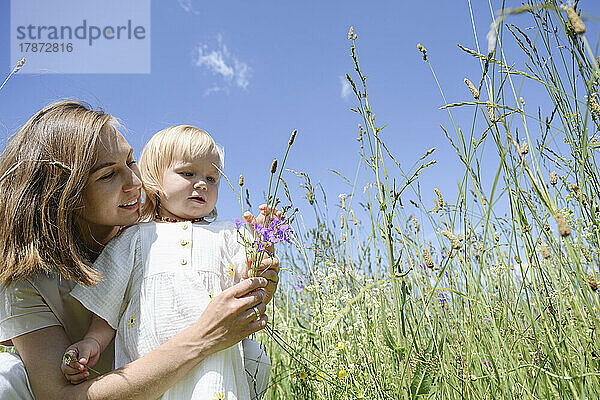 Happy mother with daughter touching flowers at field