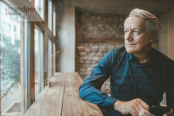 Nachdenklicher älterer Mann  der durch das Fenster im Café blickt