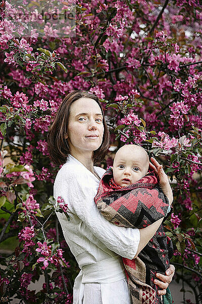 Lächelnde Frau mit kleinem Jungen steht vor einem Apfelblütenbaum