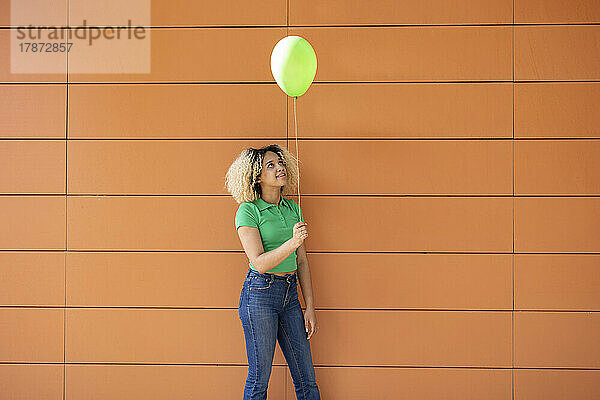 Junge Frau mit grünem Ballon steht vor der Wand