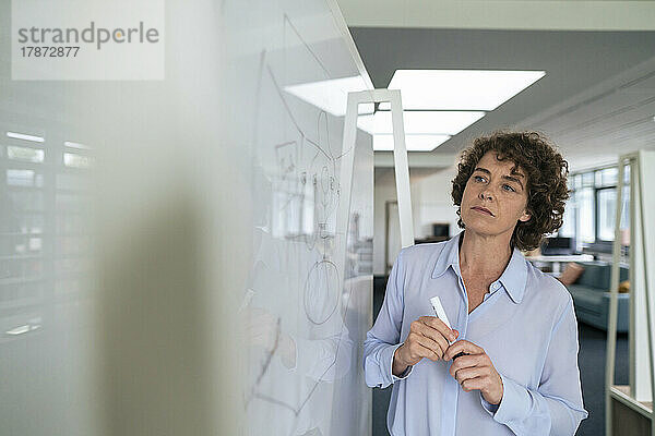 Geschäftsfrau mit lockigem Haar blickt im Büro auf das Whiteboard