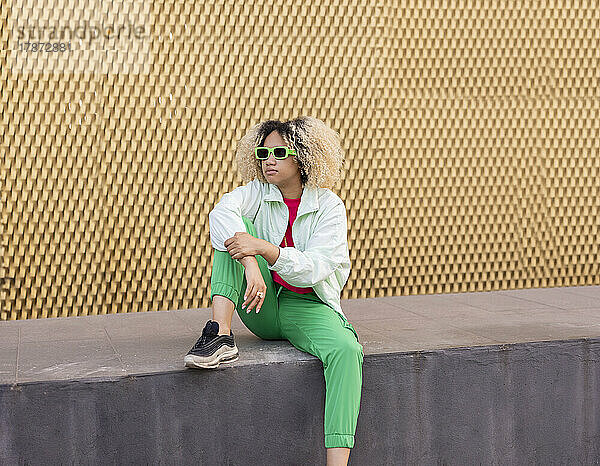 Junge Frau mit Sonnenbrille sitzt an der Wand